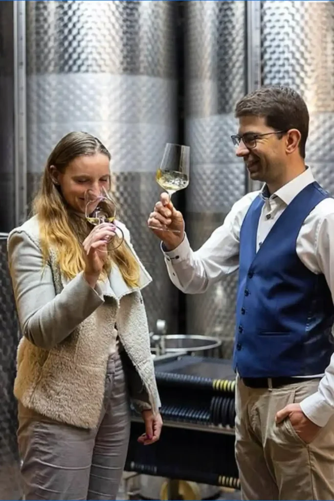 Verkostung im Weinkeller des Weinguts PAX mit zwei Personen, die Weißwein probieren.